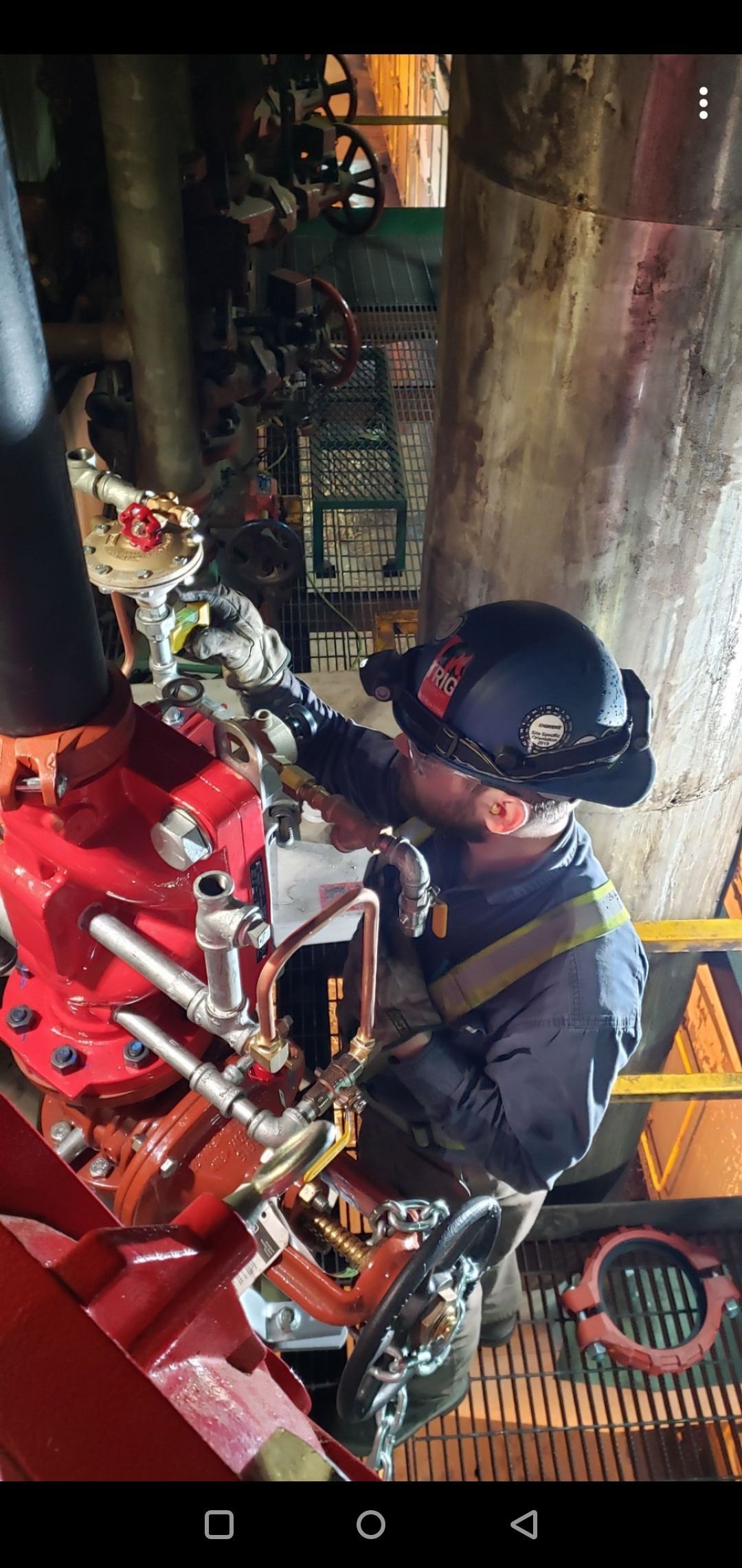 A person in a helmet working on machinery, in an industrial setting.