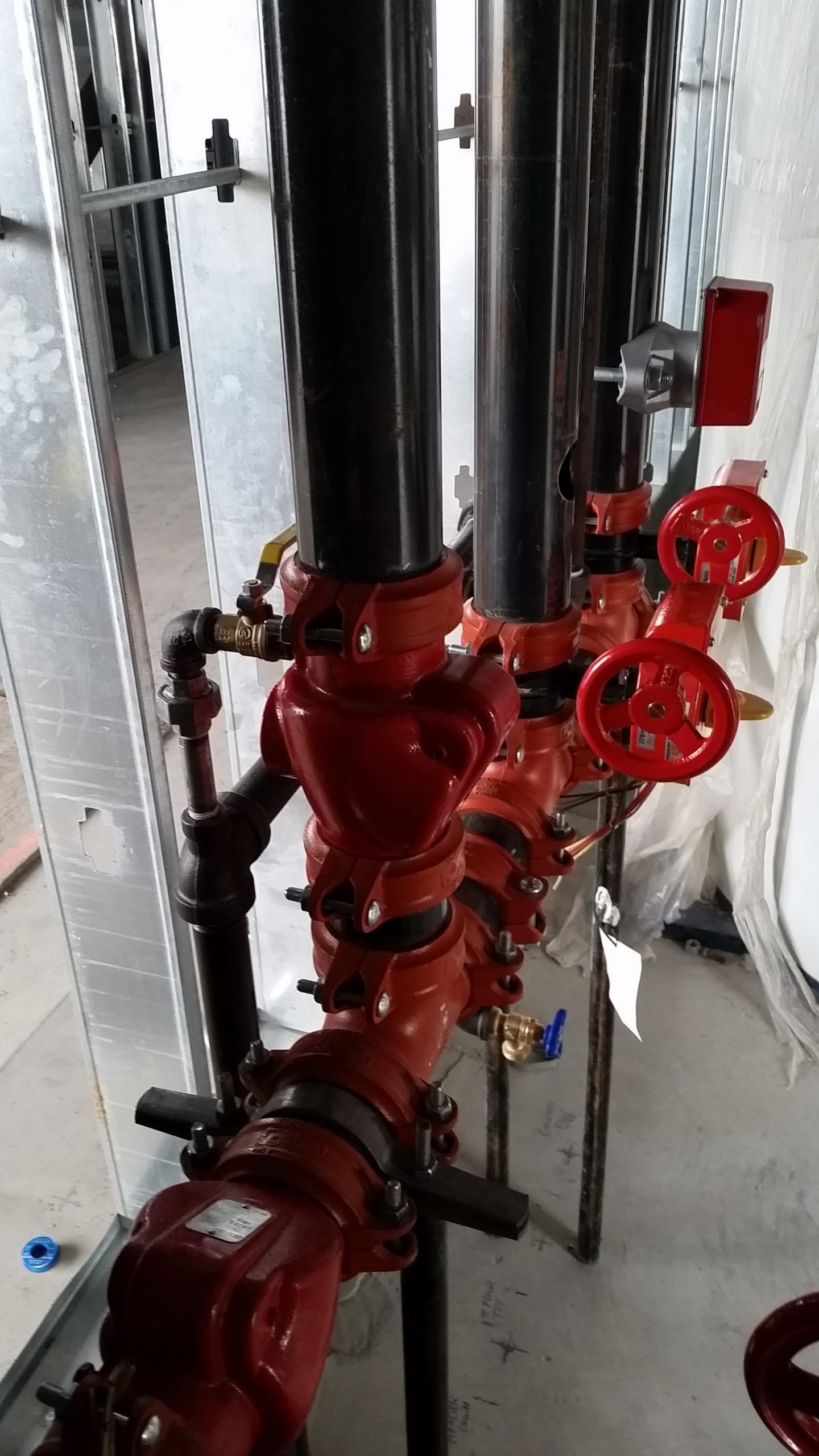 Red fire sprinkler system pipes and valves against a metal framework.