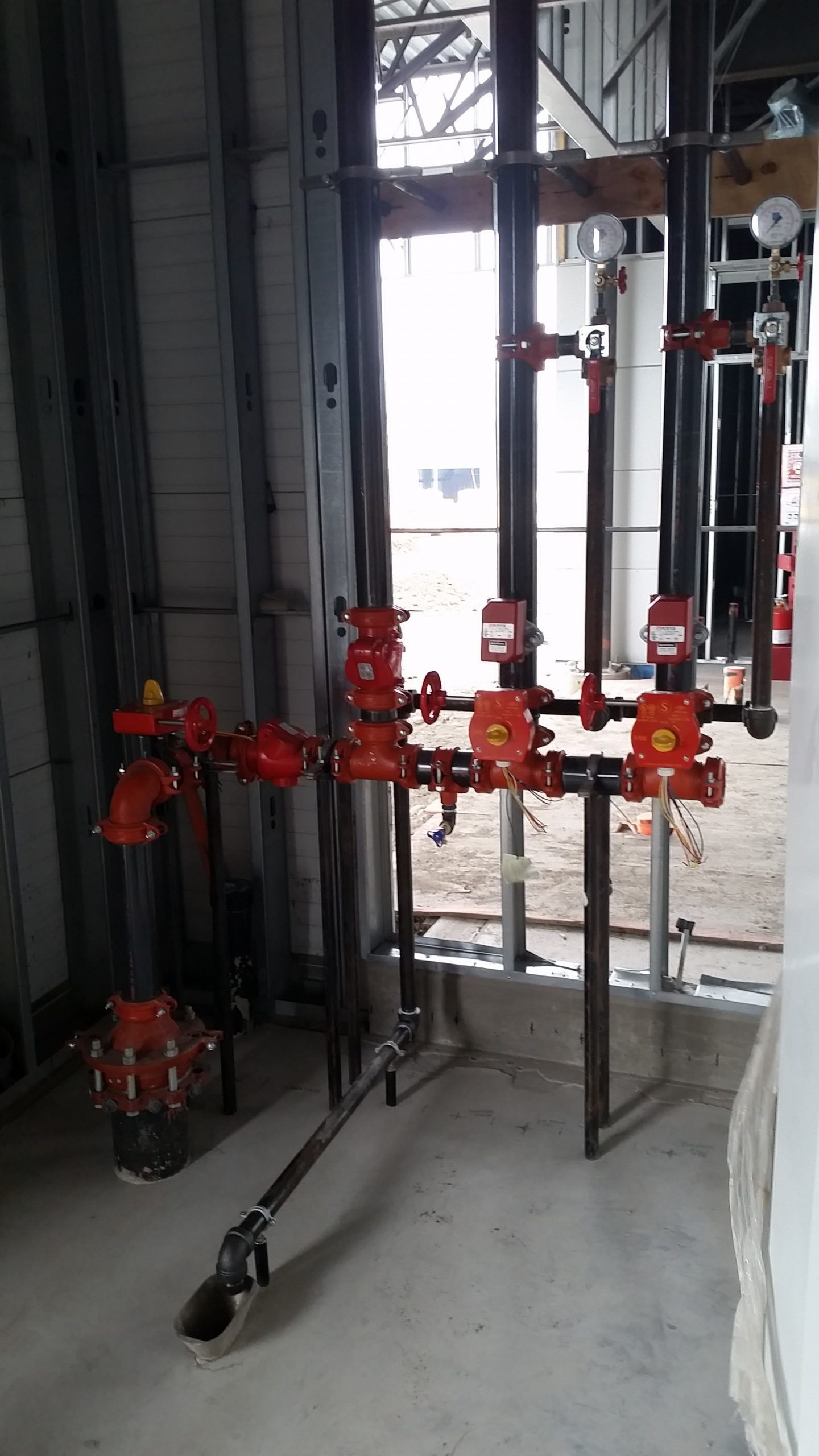 Fire sprinkler system with red valves and black pipes, under construction in a building.