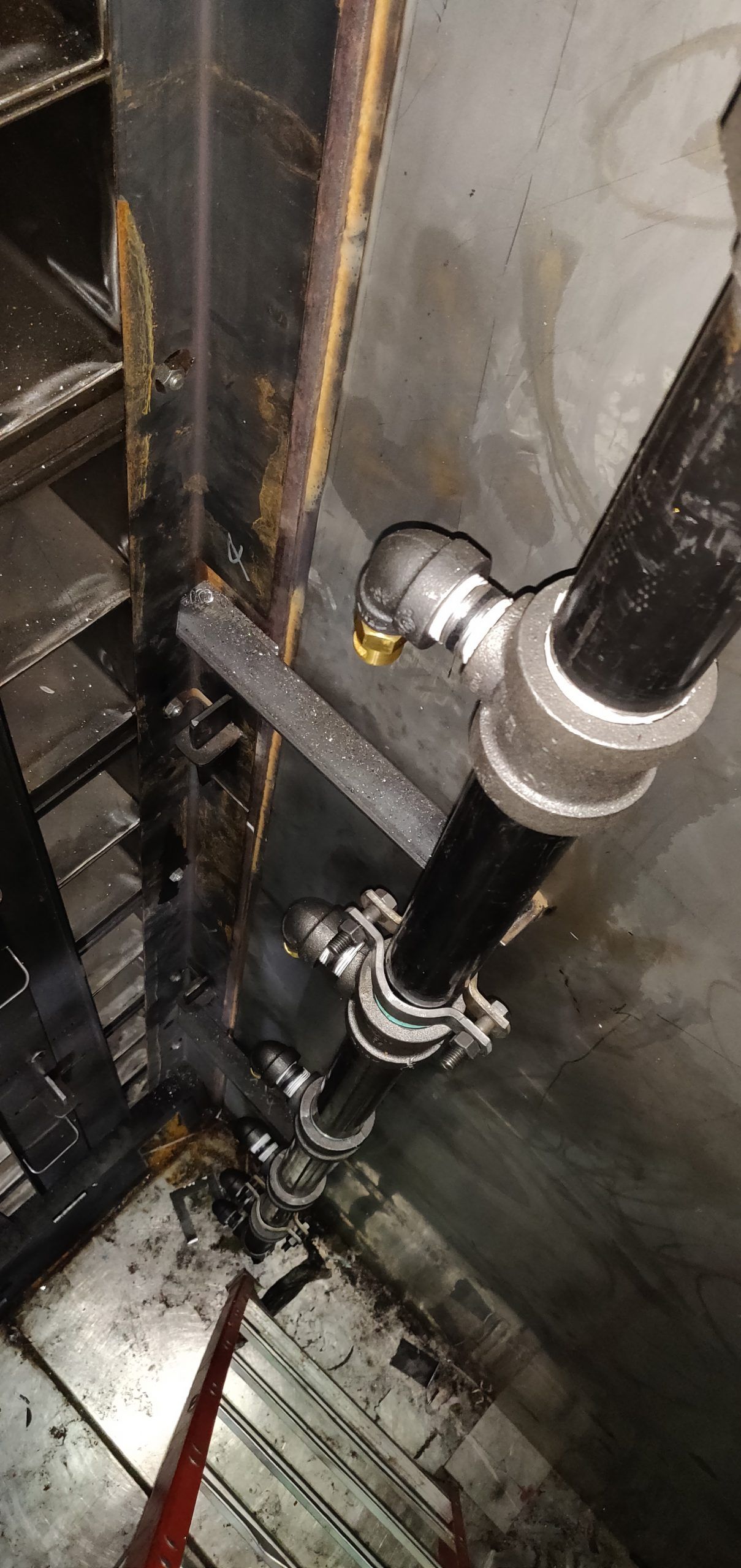 Black pipes with metal joints and clamps near a wall in a basement.