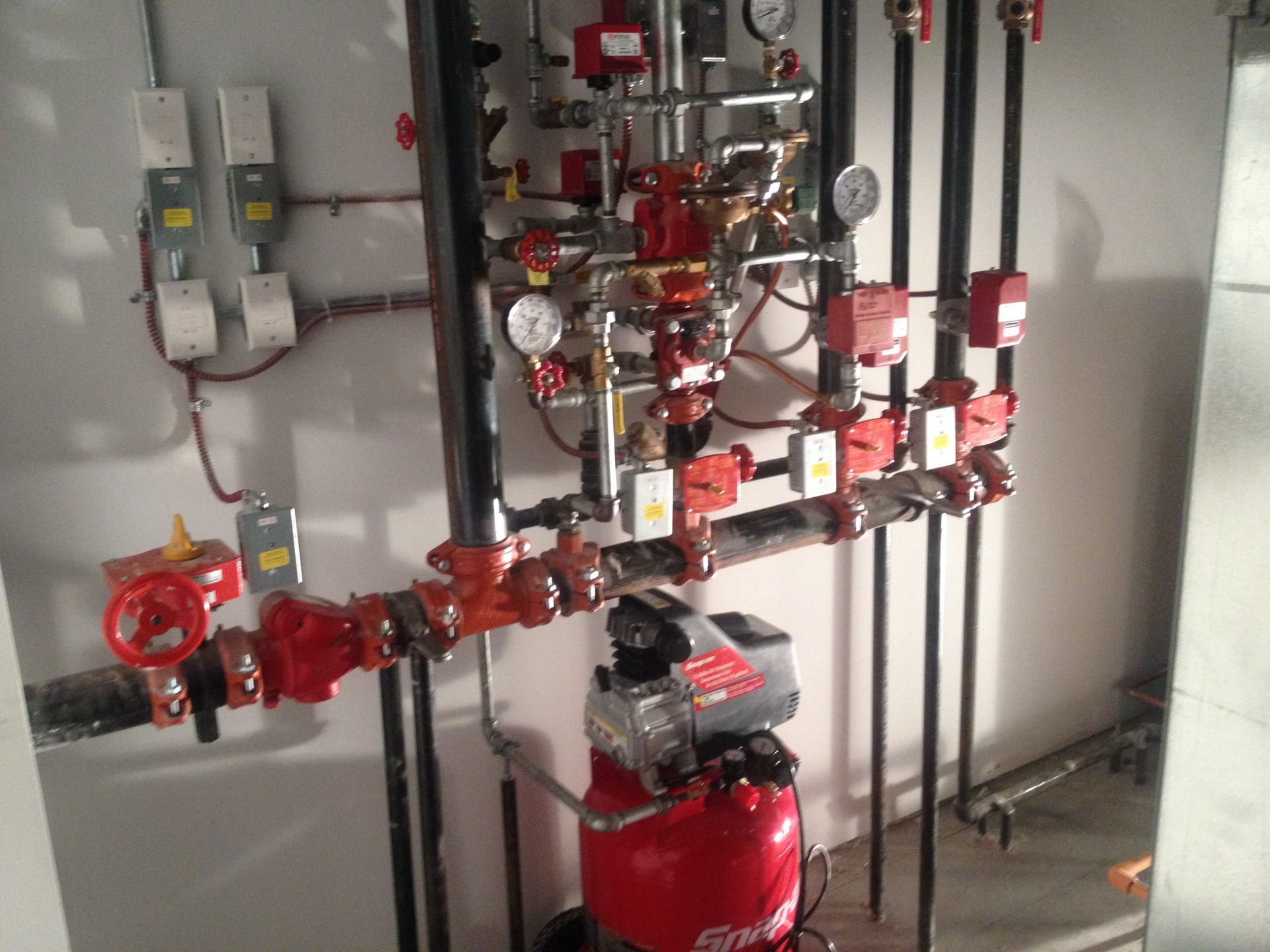 Fire sprinkler system with red pipes, valves, and gauges in a utility room.