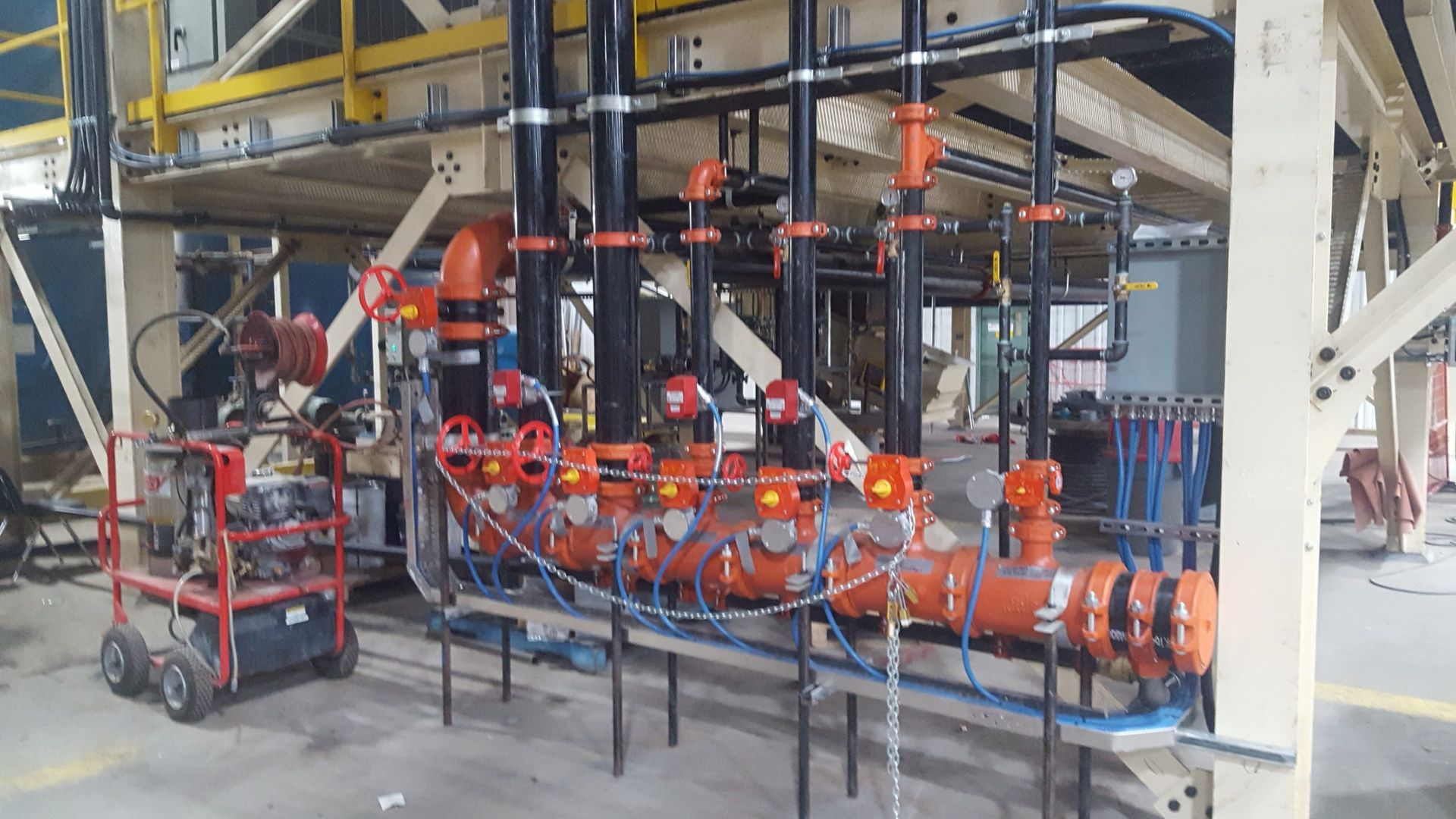 Industrial piping system with orange and black pipes, valves, and gauges in a factory setting.