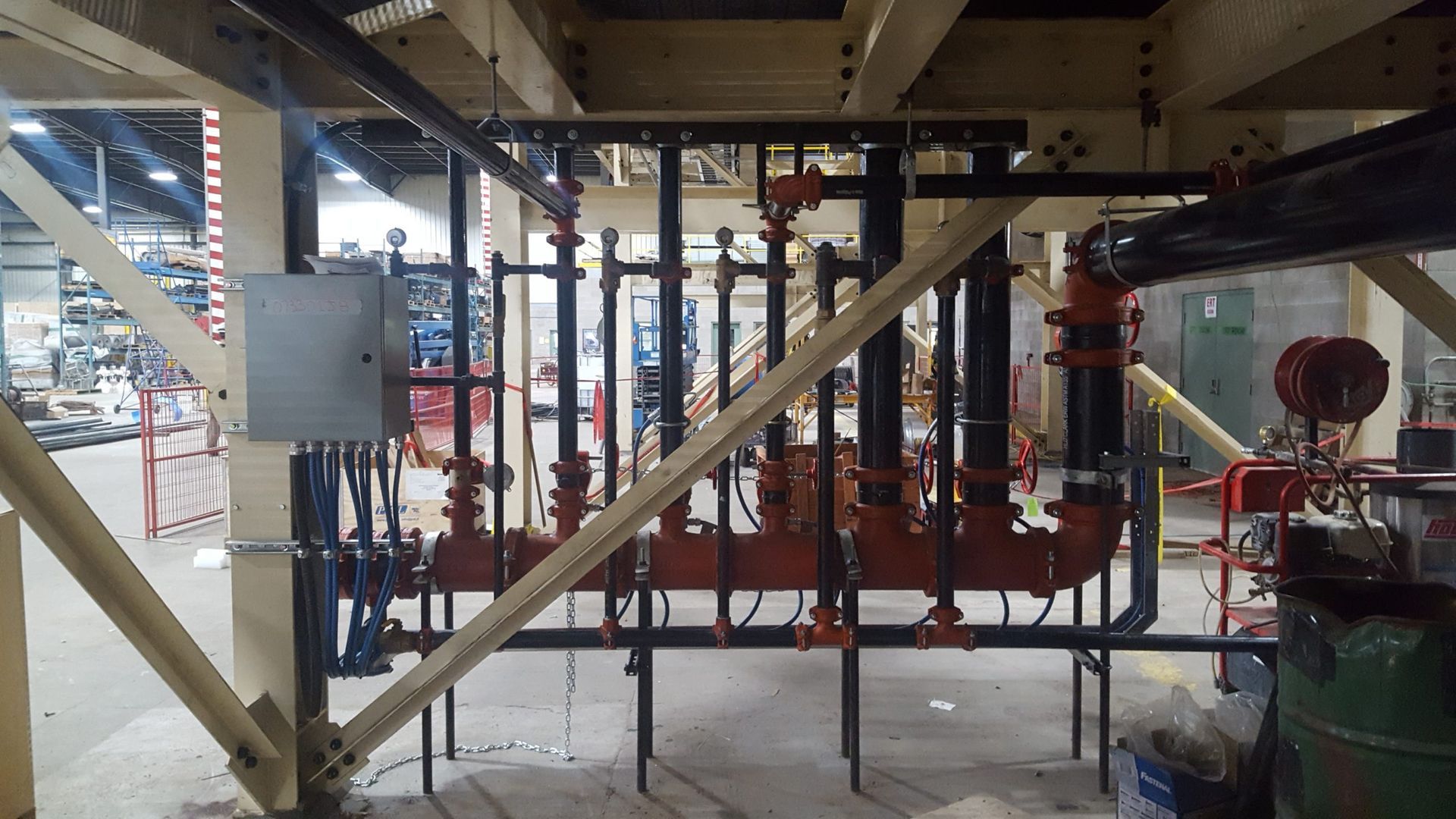 Pipes and valves, painted black and red, are arranged on a metal frame inside a building.