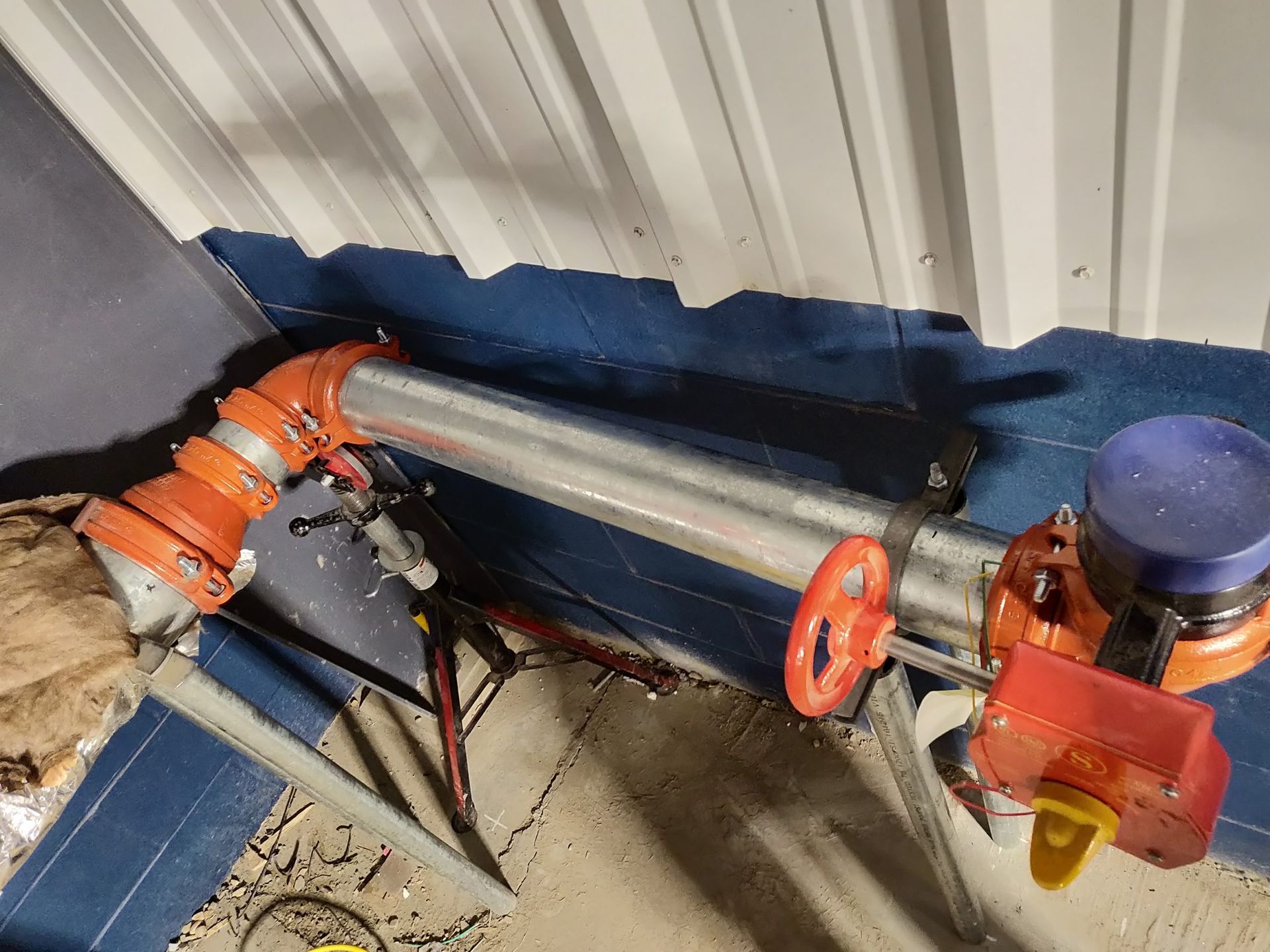 Orange and silver industrial piping and valve system near a wall.