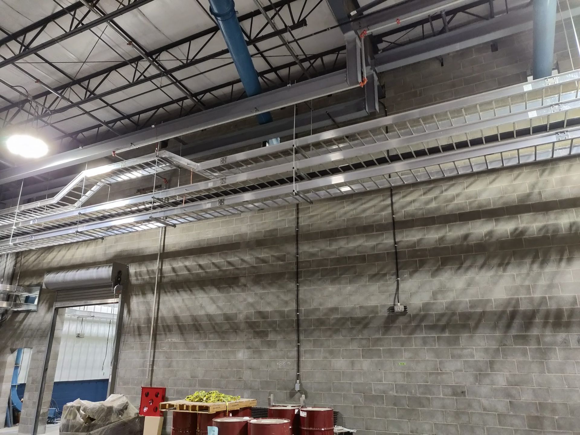 Factory interior with overhead cable trays and conduit running along a concrete block wall.
