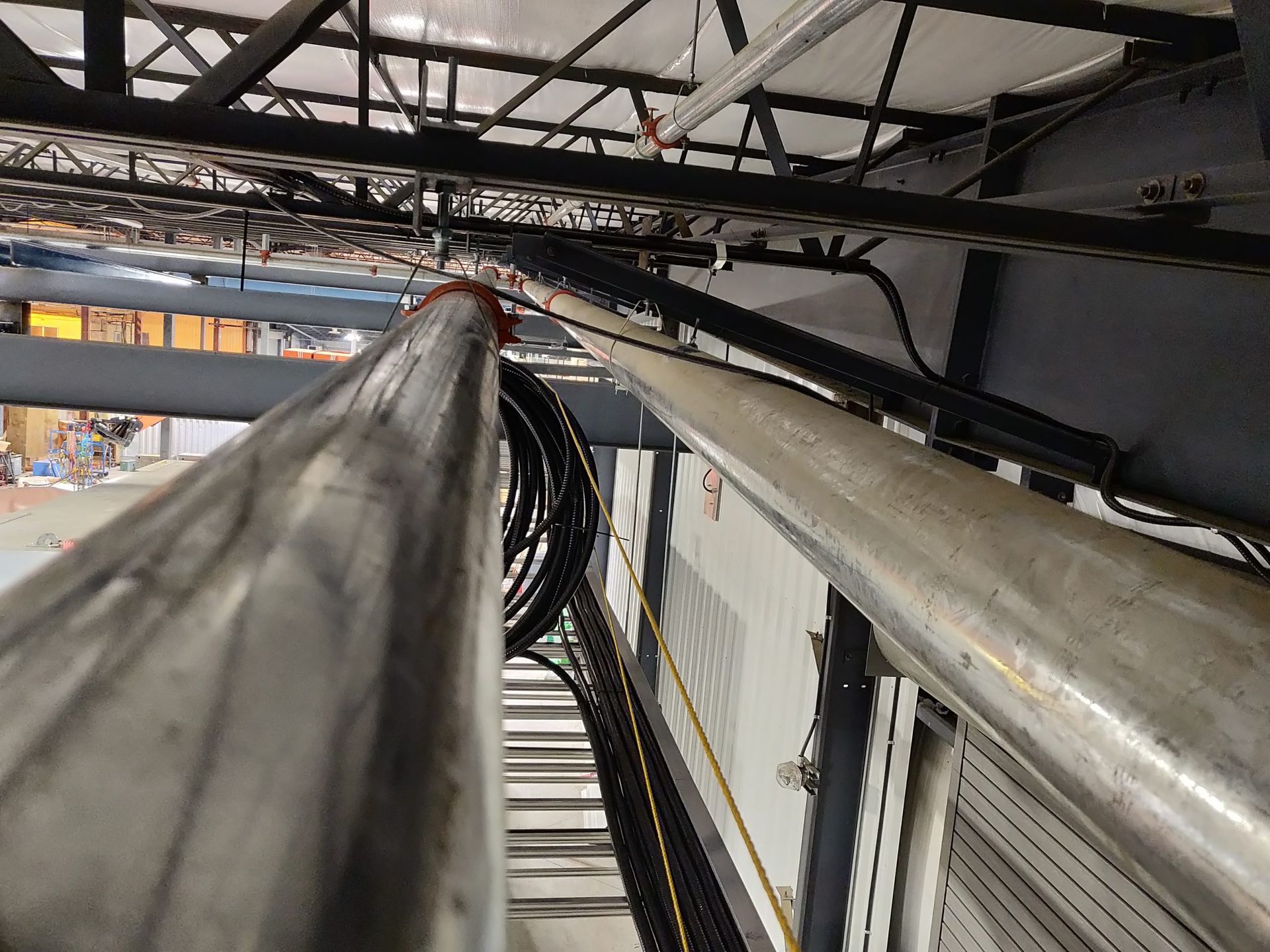 Two silver metal pipes running diagonally, with cables and supports visible above.