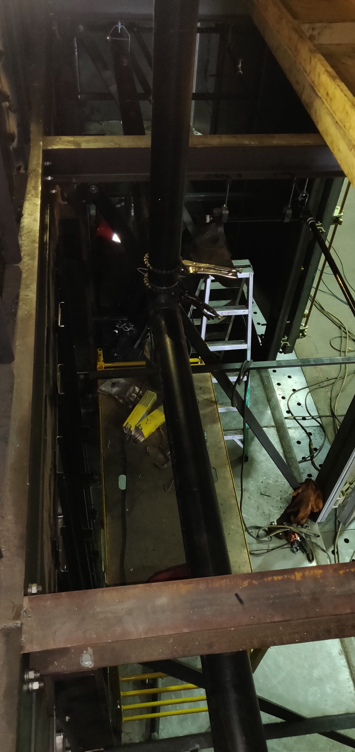 Looking down into a dark mechanical room. Metal beams and a ladder are visible.