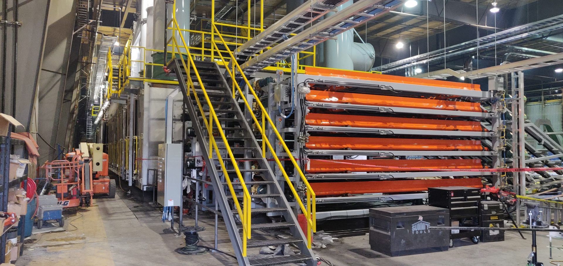 Industrial machinery with yellow safety rails and orange panels in a factory.