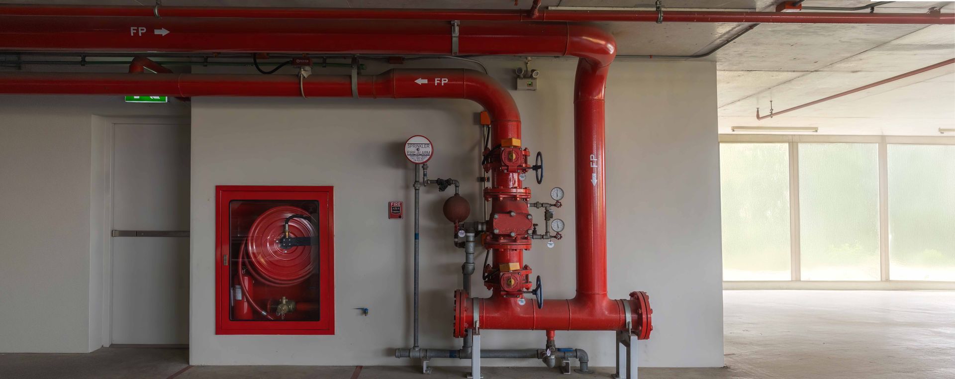 Red fire safety equipment in a white-walled room with a red fire hose cabinet and plumbing.