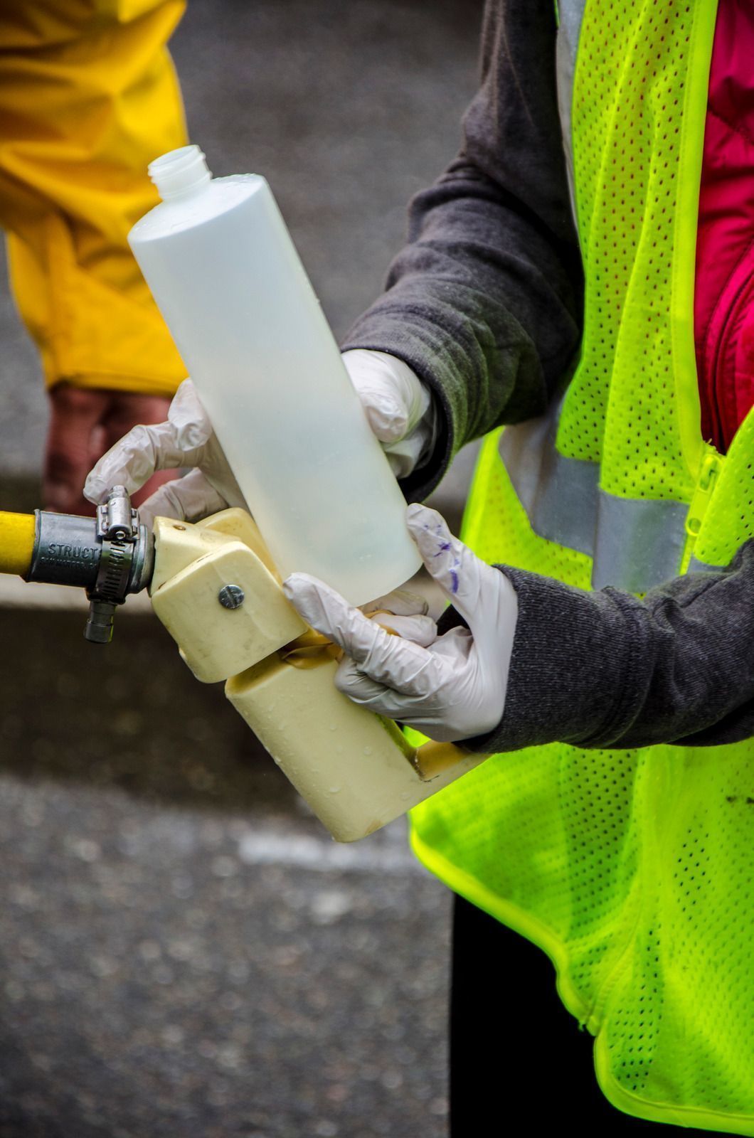 Worker in neon safety vest holding a white cylindrical tool on a street work site