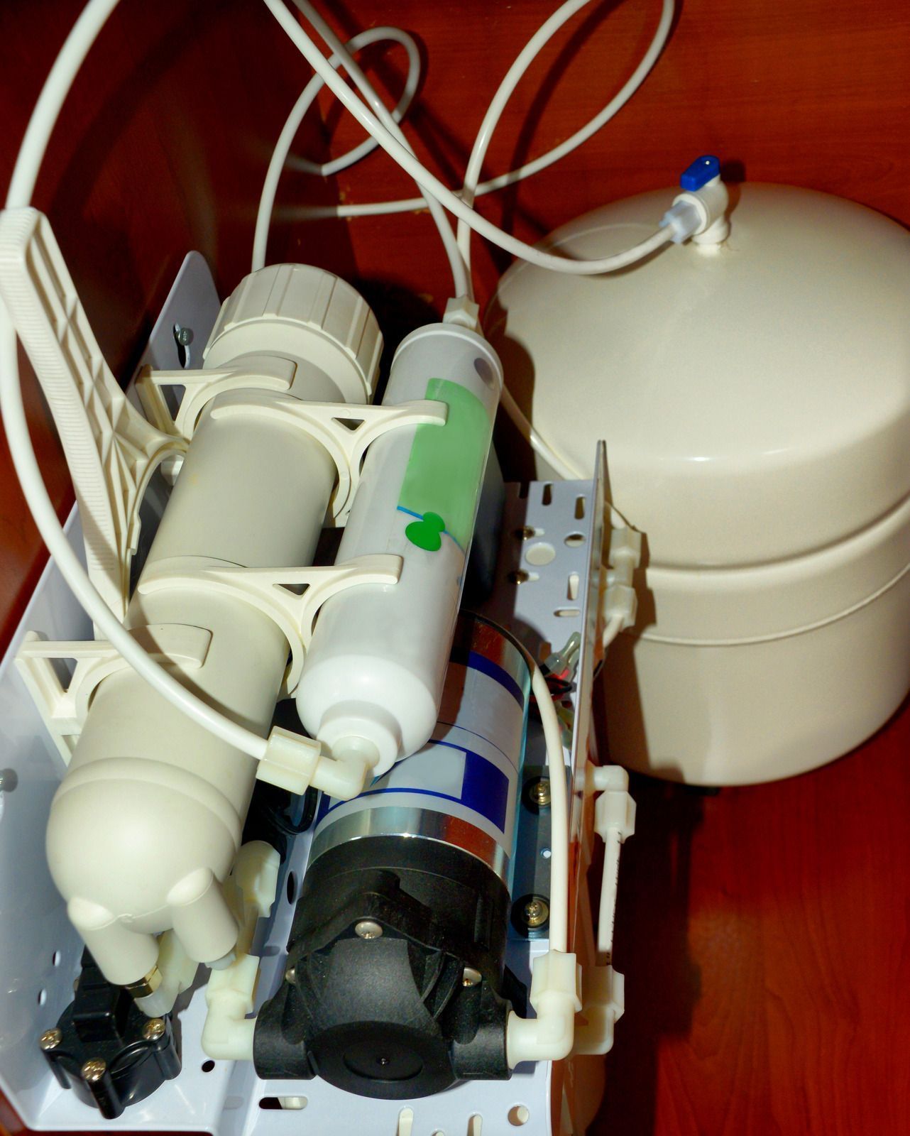 Water purification system with white cylindrical filters, tubing, and a round tank on a wooden surface