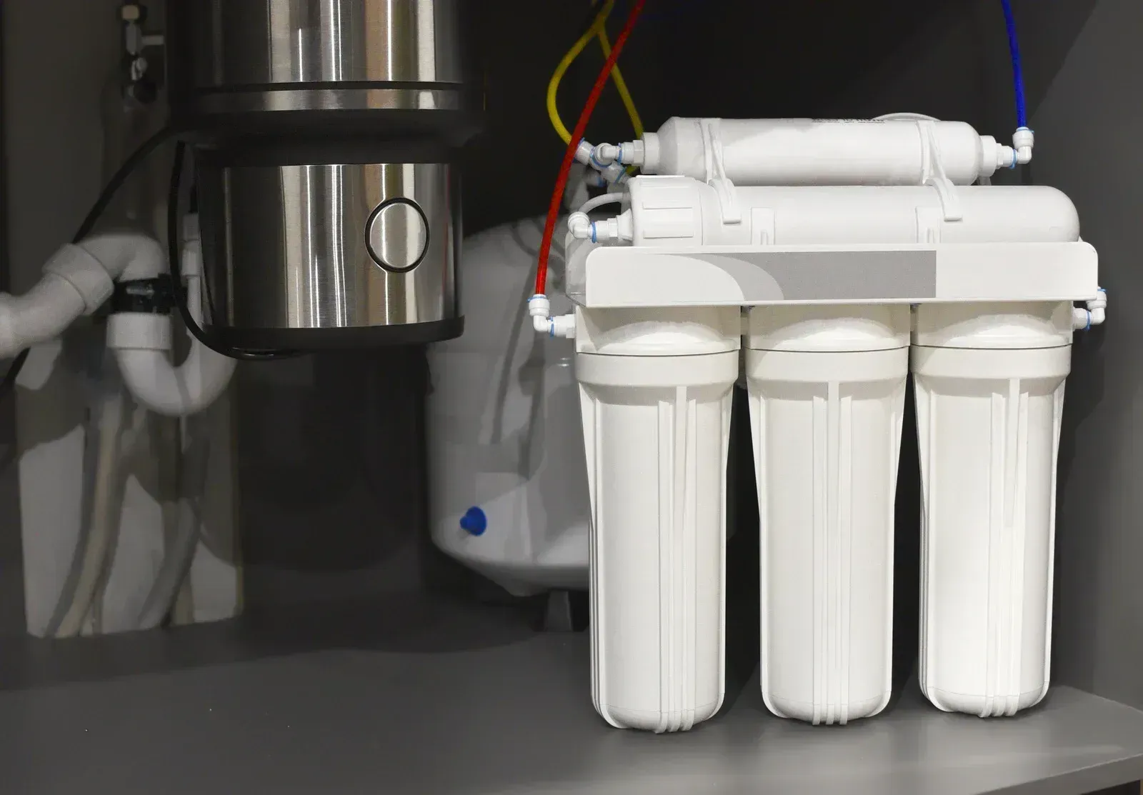 Under-sink water filtration system with three white filter cartridges and stainless steel components
