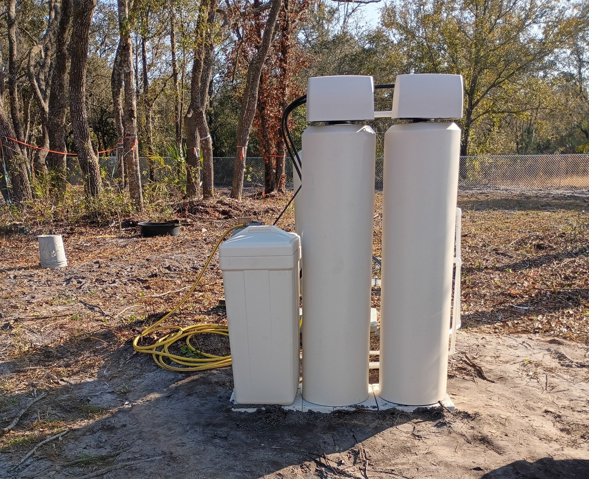Outdoor utility equipment with two white pipes and a beige box near a wooded area