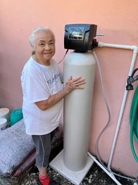 Woman standing beside a water softener tank against a pink wall