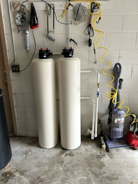 Two tall white water softener tanks in a garage with hoses and tools on the wall