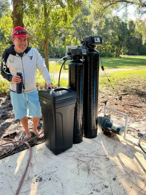 Person standing beside outdoor water filtration tanks on a concrete pad in a grassy yard