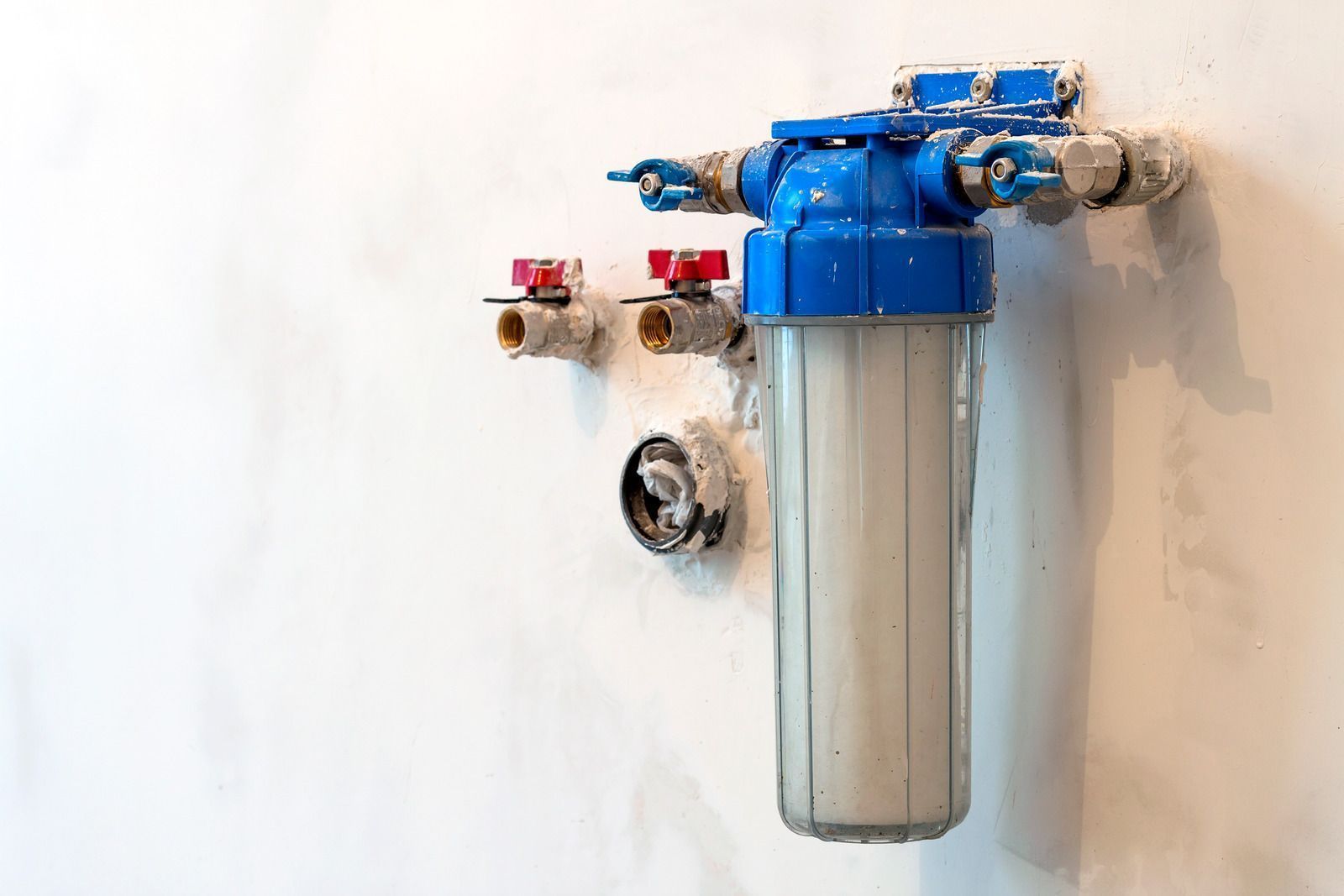 Blue water filter unit mounted on a white wall with visible valves and tubing