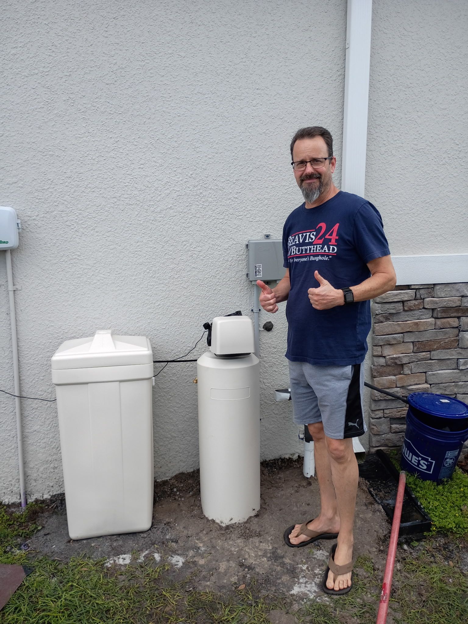 Two black utility tanks beside a stucco wall, connected by pipes and a hose.