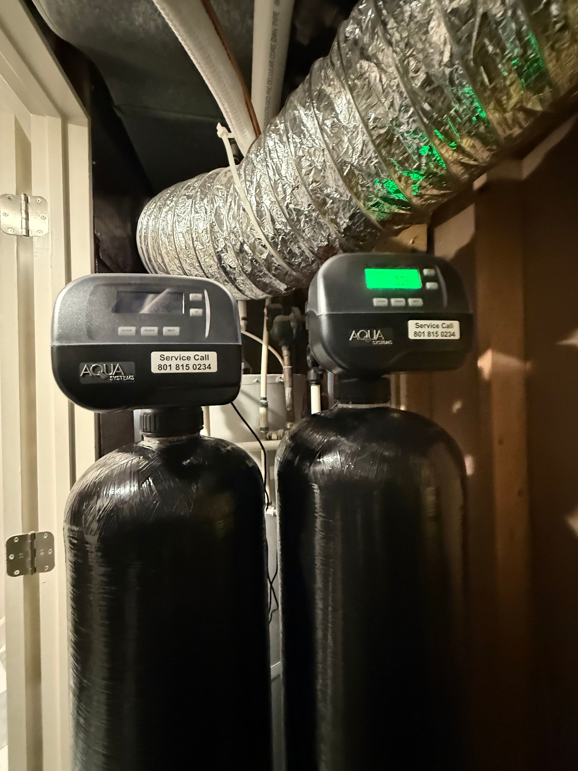 Two black water softener tanks in a utility closet with silver ductwork overhead