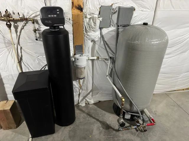 Water softener and whole-house filtration system with black and gray tanks in a utility room.