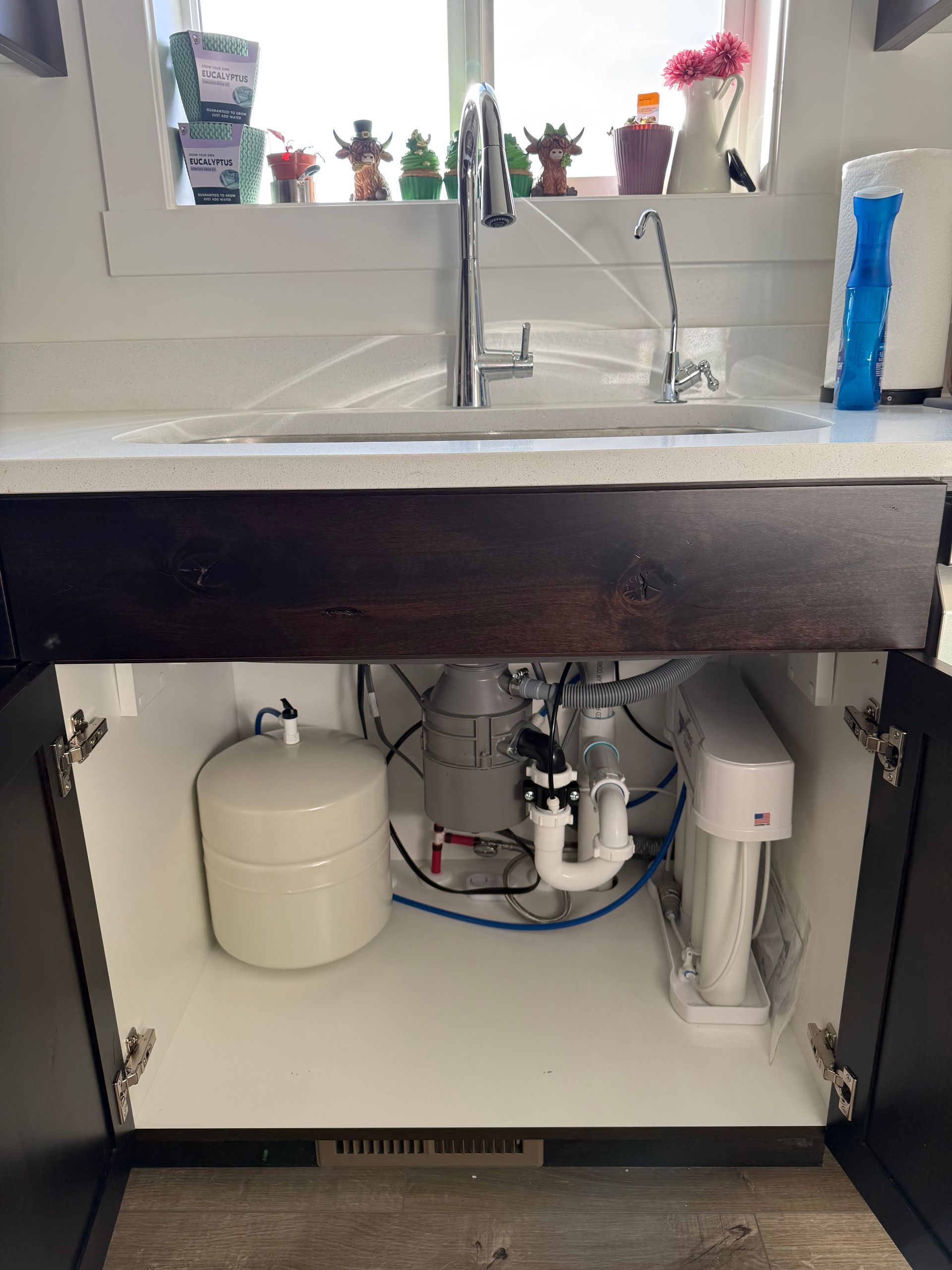 Under-sink cabinet with plumbing, water filter tanks, and pipes beneath a kitchen sink