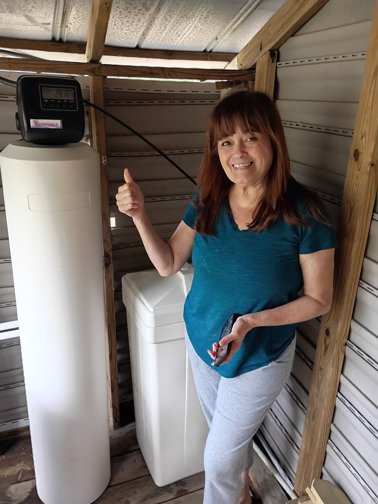 Woman in a shed beside a water heater and washing machine, giving a thumbs-up.