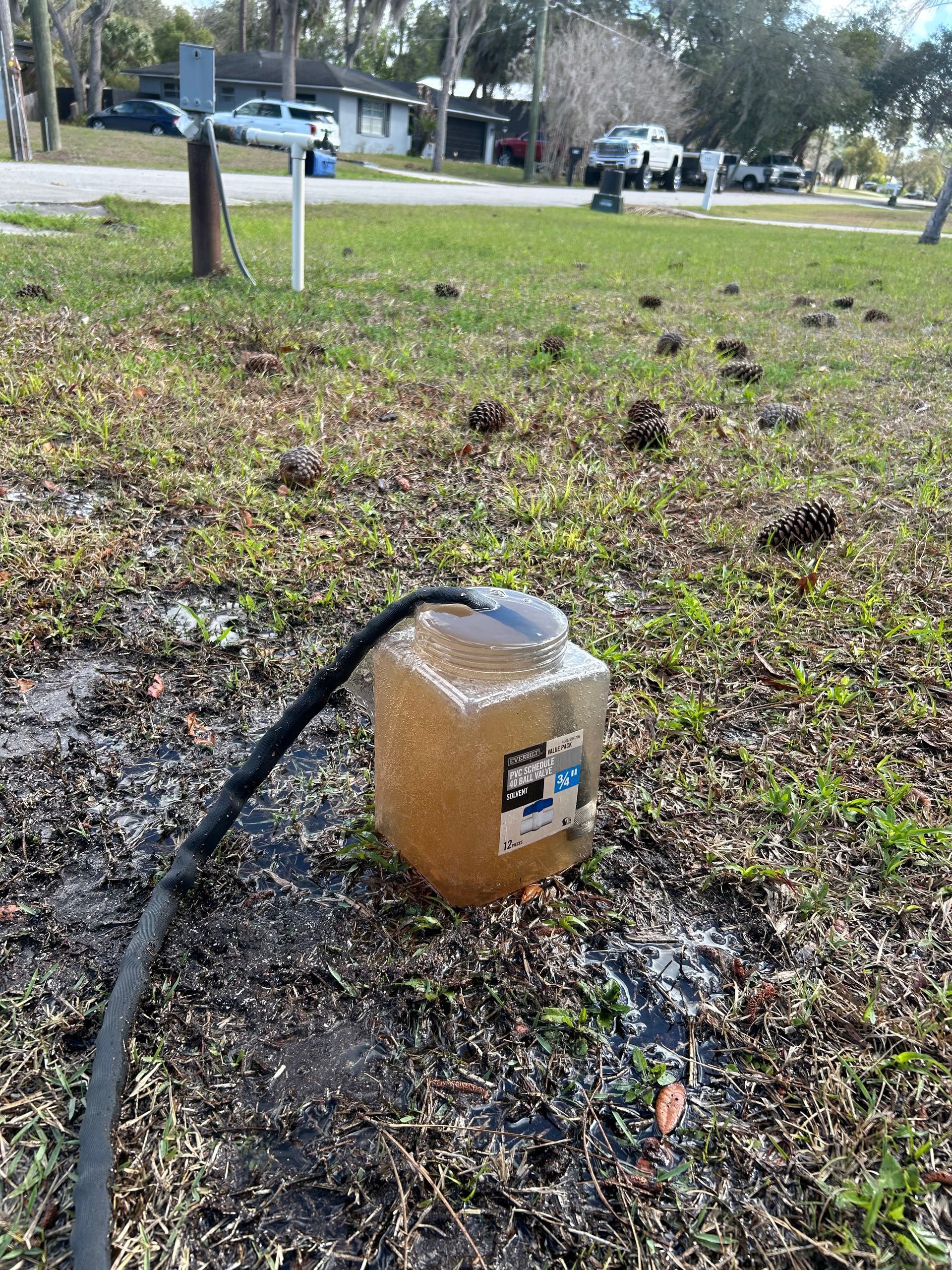 Damaged utility box with black cable on a grassy roadside near parked cars and trees