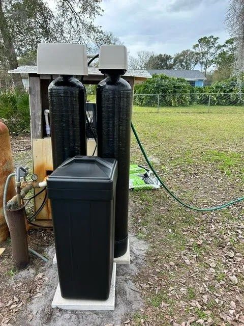 Two black water treatment tanks and a control box outdoors on a grassy lot