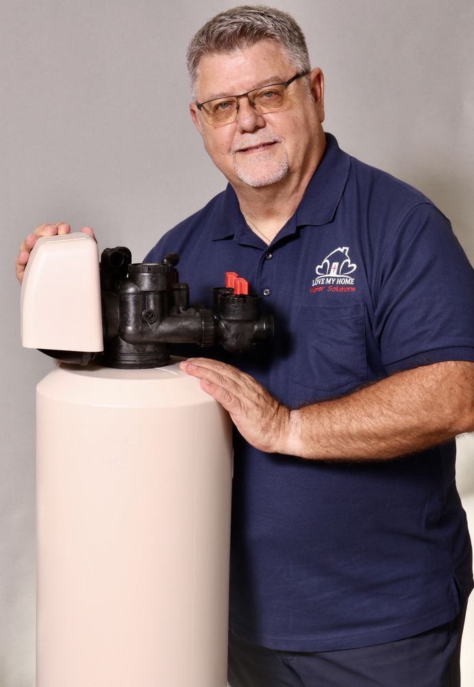 Man holding a water softener tank with a control head, wearing a navy polo shirt.