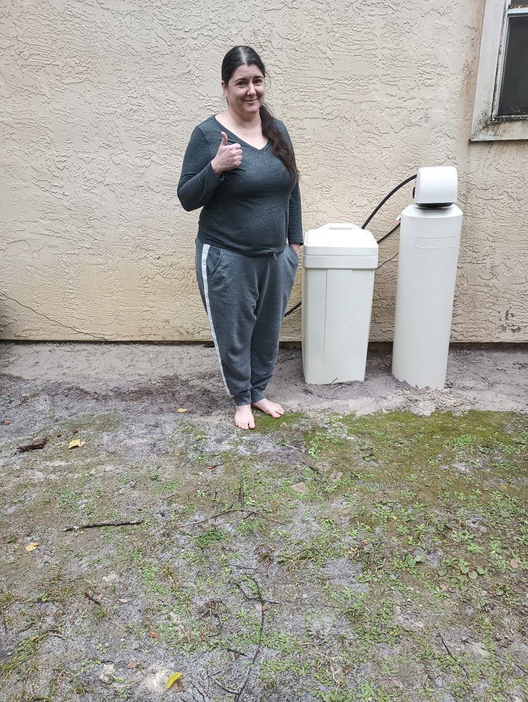 Woman standing outdoors beside two white trash bins against a beige wall.