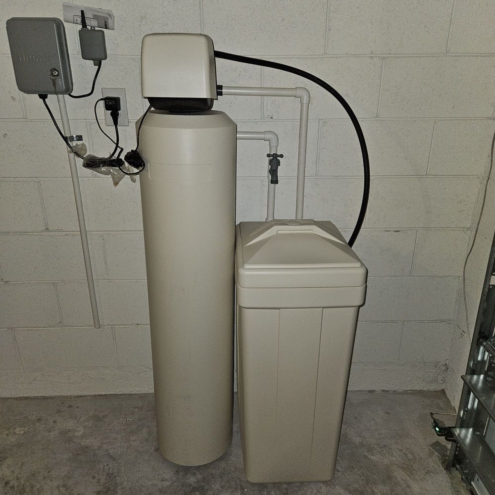 Water softener system with tall beige tank and cabinet in a utility room against a tiled wall