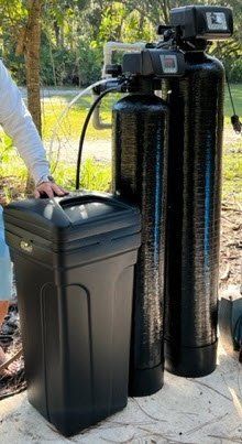 Black water filtration tank beside a gray trash bin on a concrete pad outdoors