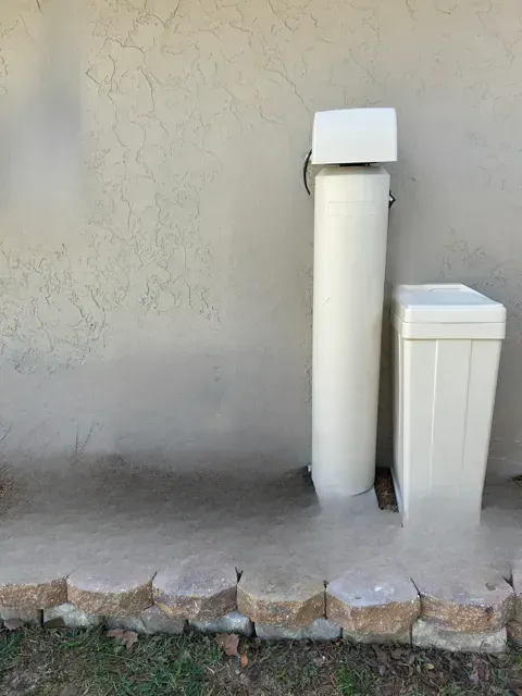 Stone walkway beside a beige wall with a white pipe and utility box.