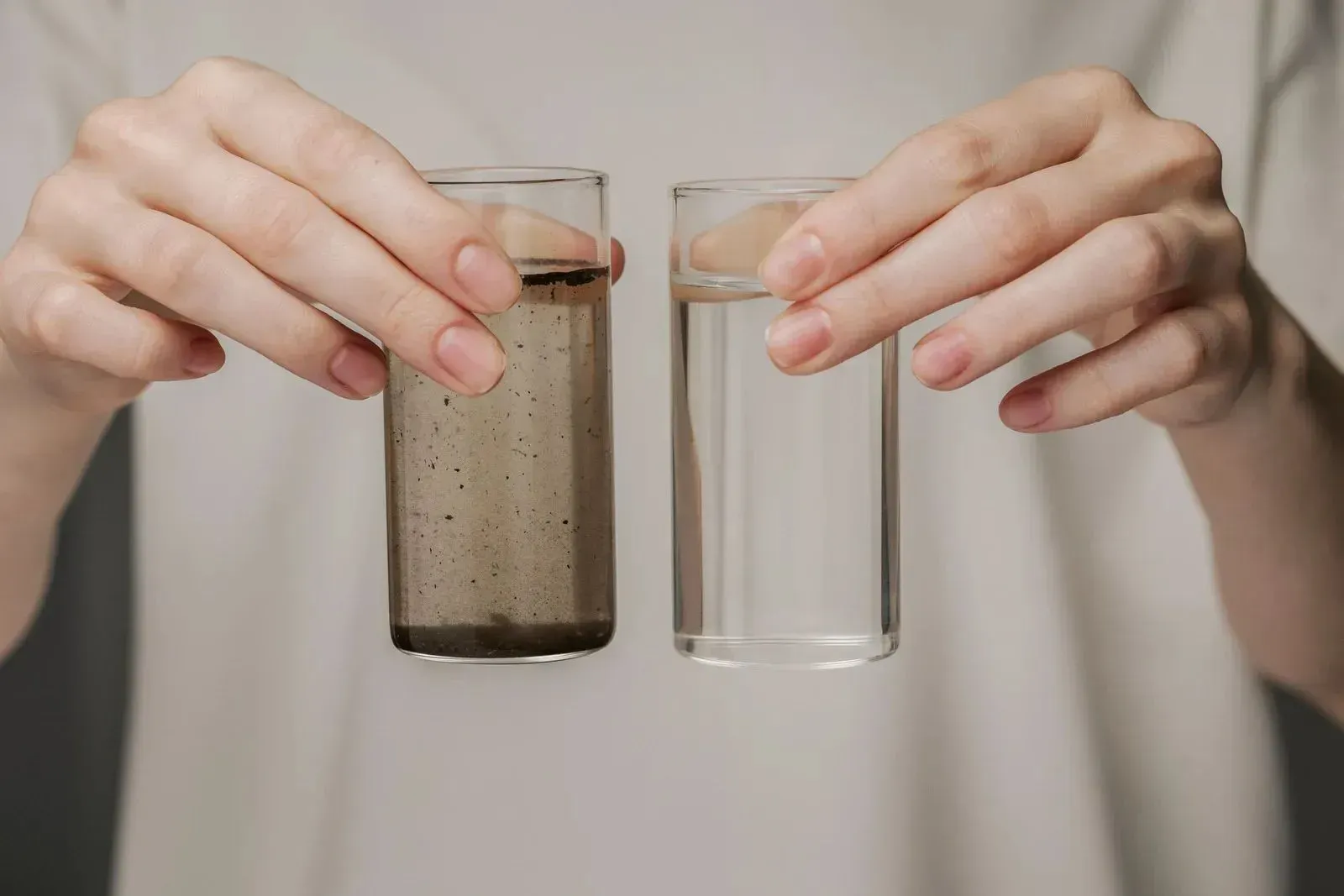 Hands holding two glasses, one cloudy and one clear, comparing water quality