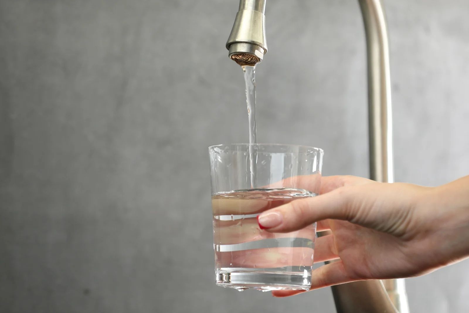 Hand filling a clear glass with water from a kitchen faucet