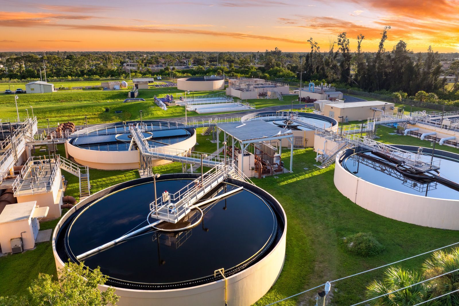 Aerial view of a water treatment plant with large circular tanks at sunset
