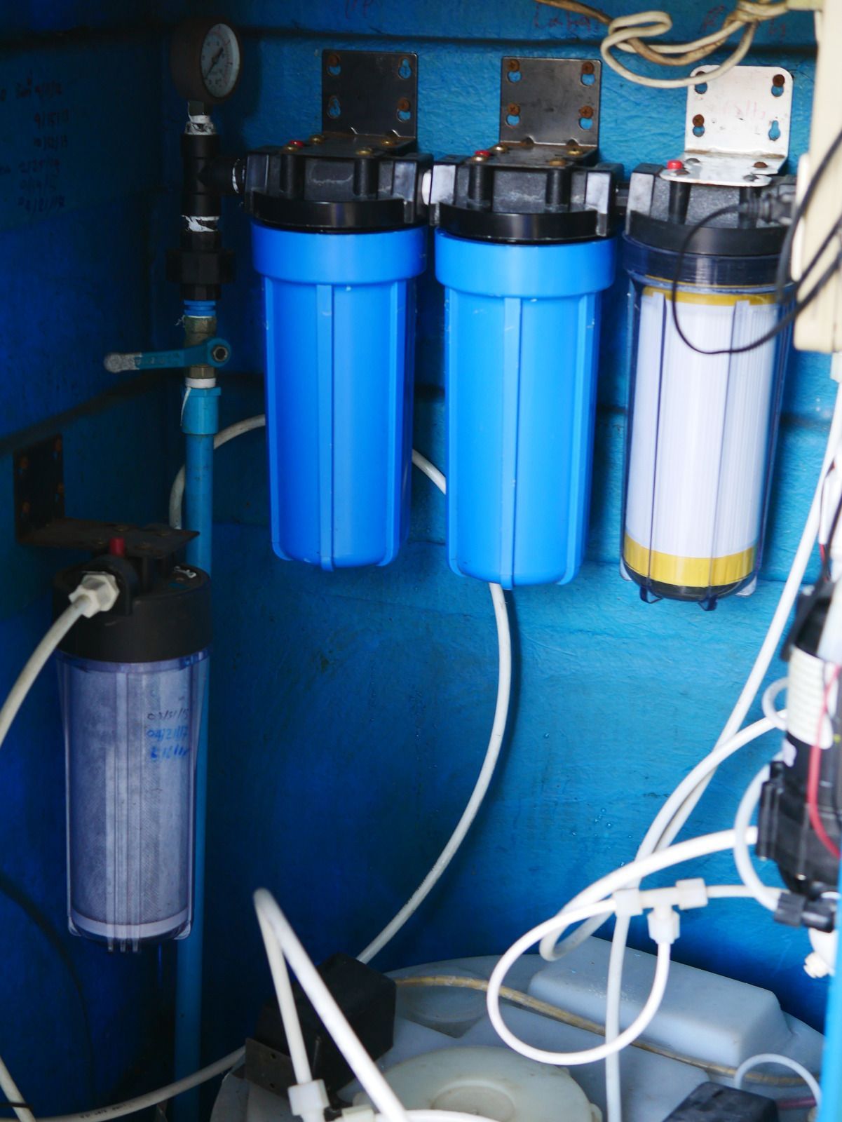 Blue and white water filtration system with multiple canisters and tubing in a utility space