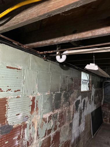 Flood-damaged basement wall with peeling paint, exposed beams, and hanging light fixtures.