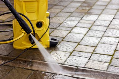 Pressure washer spraying water on a stone patio beside a yellow machine