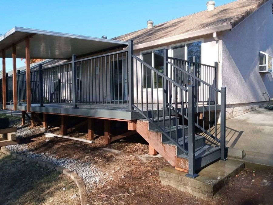 A deck with gray railings and a metal cover attached to the back of a light-colored house, featuring stairs leading down.