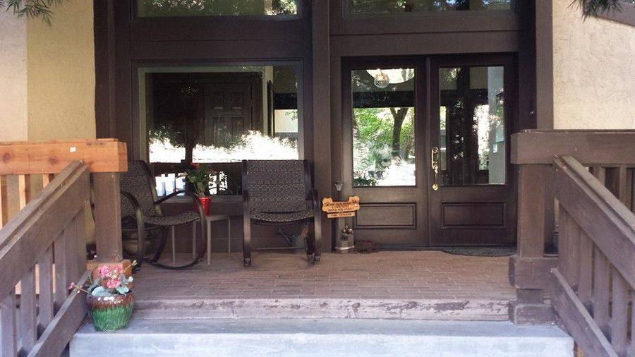 A porch entrance with a wooden railing, two outdoor rocking chairs, and dark brown double doors.