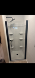 Glass shower stall with a black-framed door and white corner shelves inside.