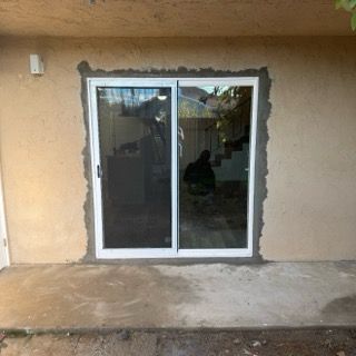 Sliding glass patio door framed by unfinished stucco wall on a concrete patio
