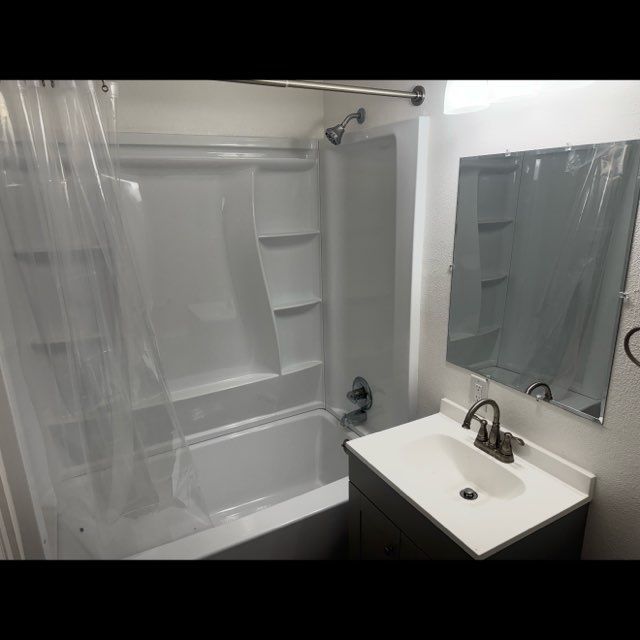Small bathroom with shower-tub, clear curtain, white sink, mirror, and dark vanity.