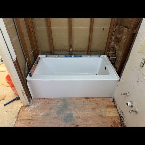Unfinished bathroom with a white bathtub installed against exposed wall studs and plywood subfloor
