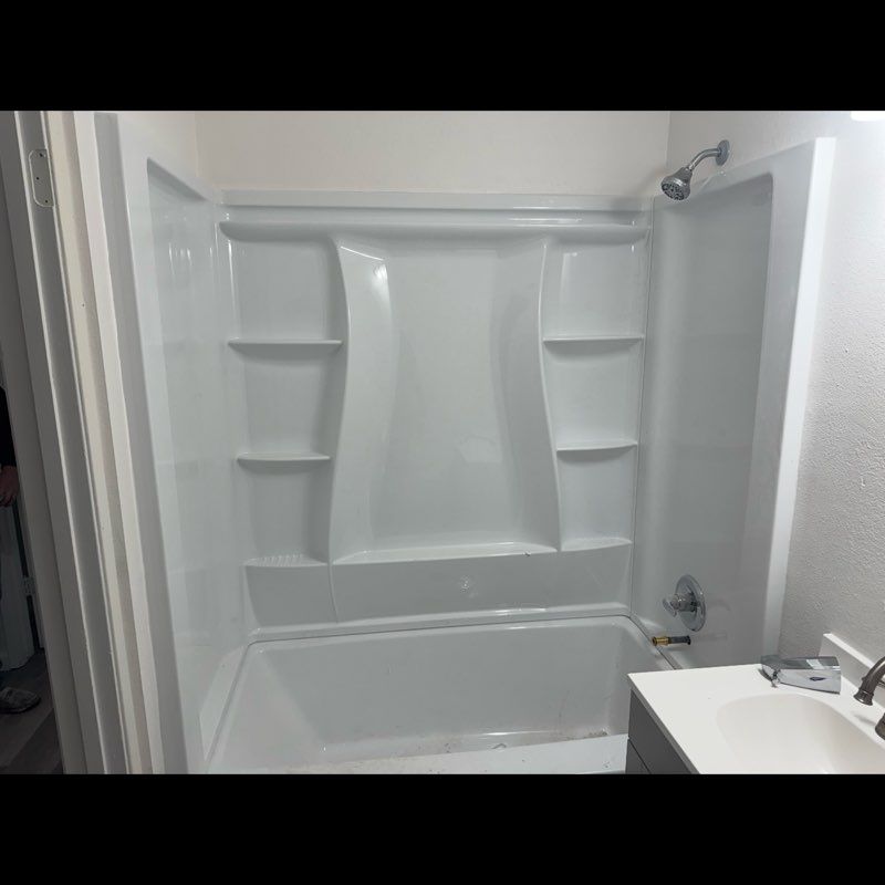 Small white bathroom with a built-in bathtub and shower surround, plus a sink on the right.