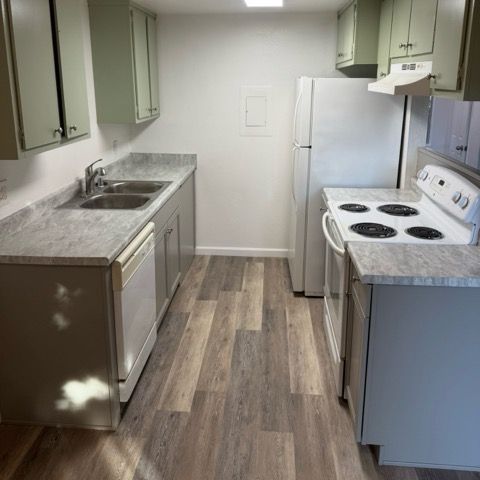 Small kitchen with white appliances, green cabinets, and wood-look flooring.