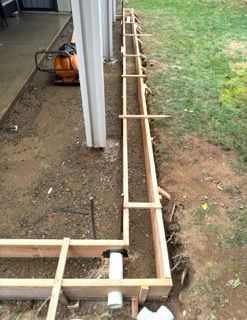 Wooden formwork framing a narrow concrete trench beside a house and lawn.