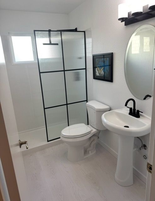 Modern white bathroom with glass shower, toilet, pedestal sink, and oval mirror.