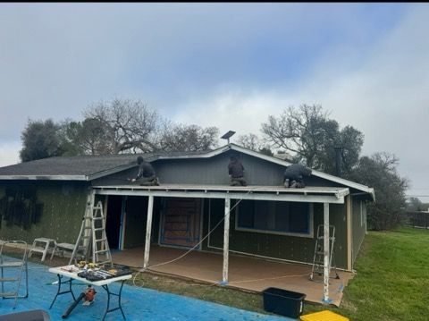 House under construction with white porch posts, ladders, and blue tarps in the front yard.